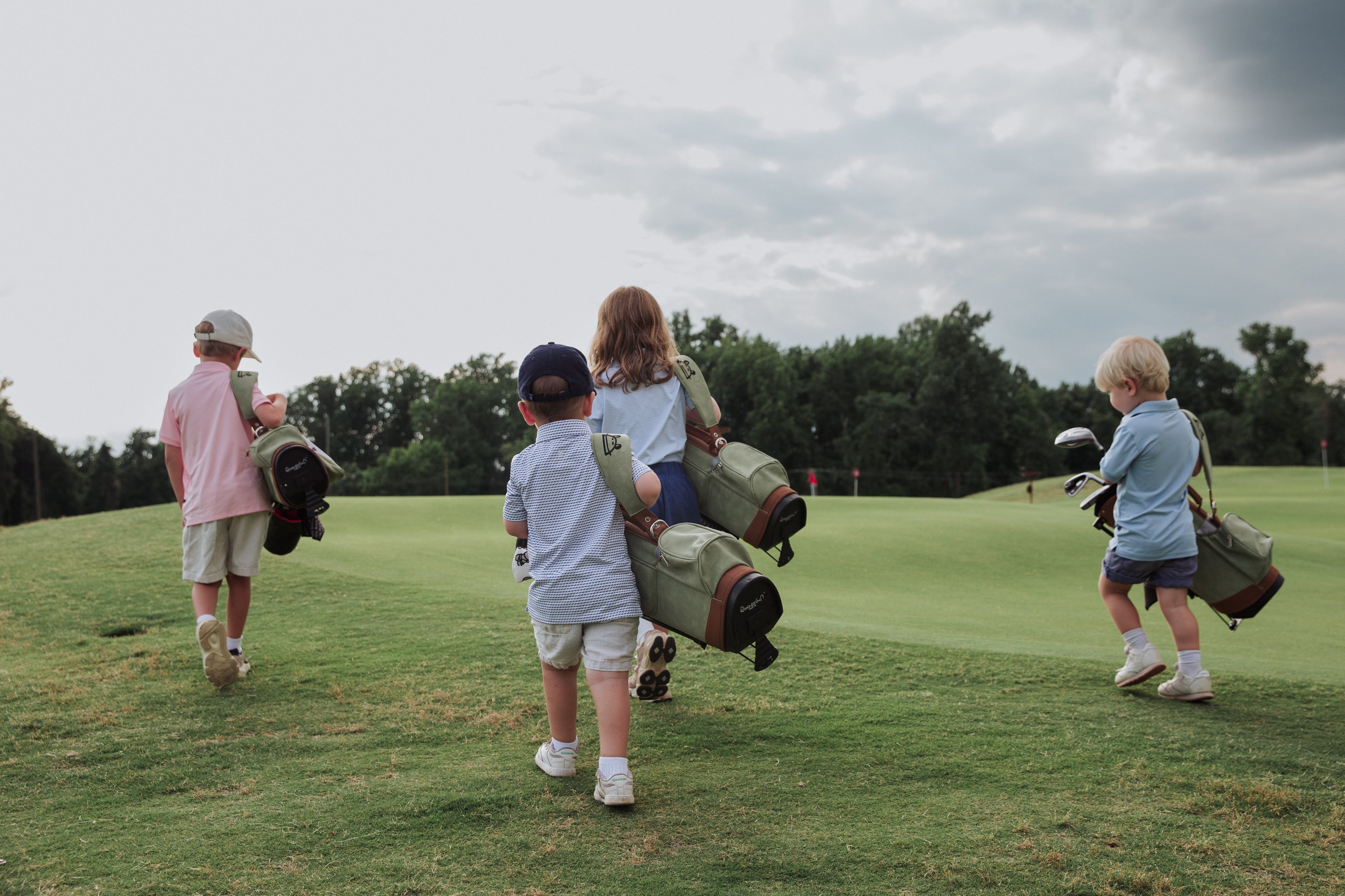 Four children walking on a golf course with golf bags.
