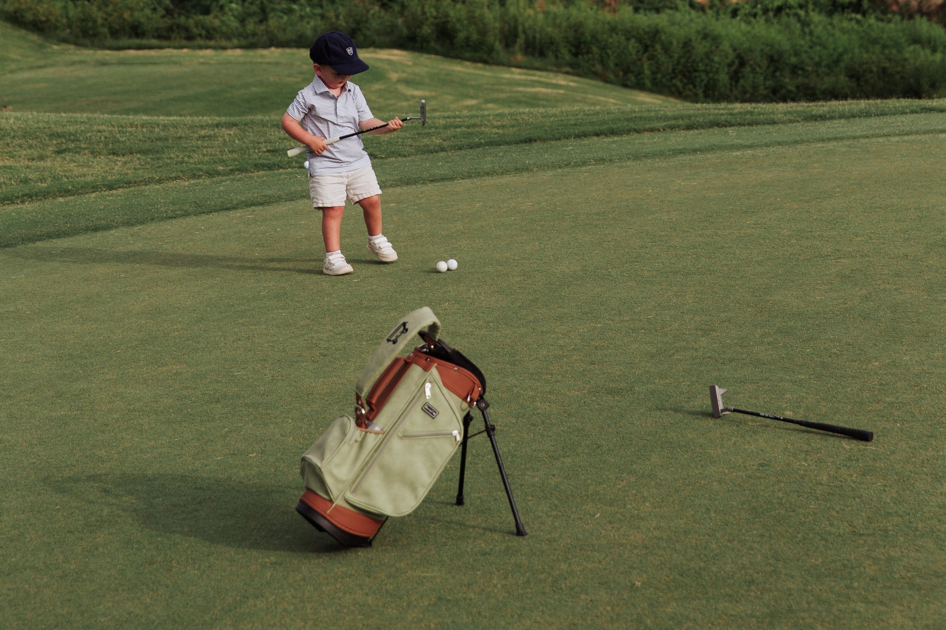 Child playing golf on a green course with a fence and trees in the background